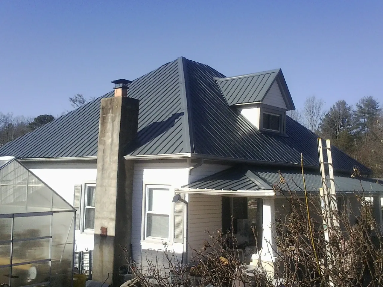 Dark blue standing seam metal roof on a white farmhouse with dormer — Slate & Tile Roof Repair by Roofing Brothers in Huron