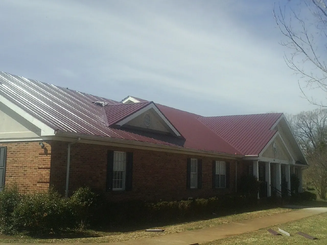 Red metal roof with gabled entries on a long brick building, from a Hail Damage Roof Repair job in Huron