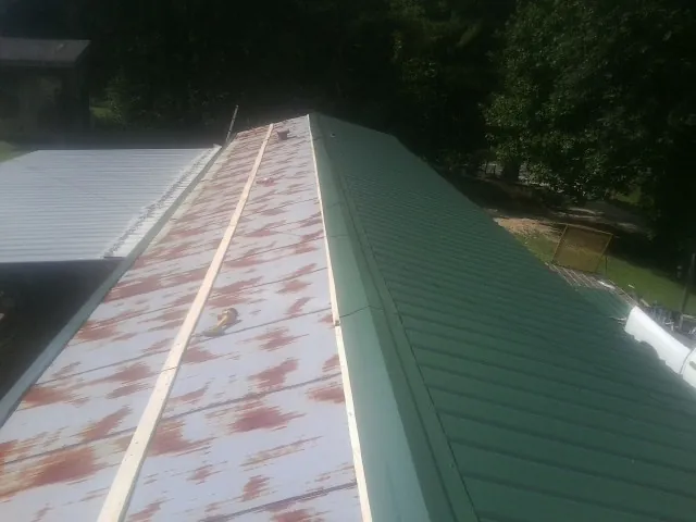 Old rusted panels beside newly installed green metal roofing — Wind Damage Roof Repair by Roofing Brothers in Huron