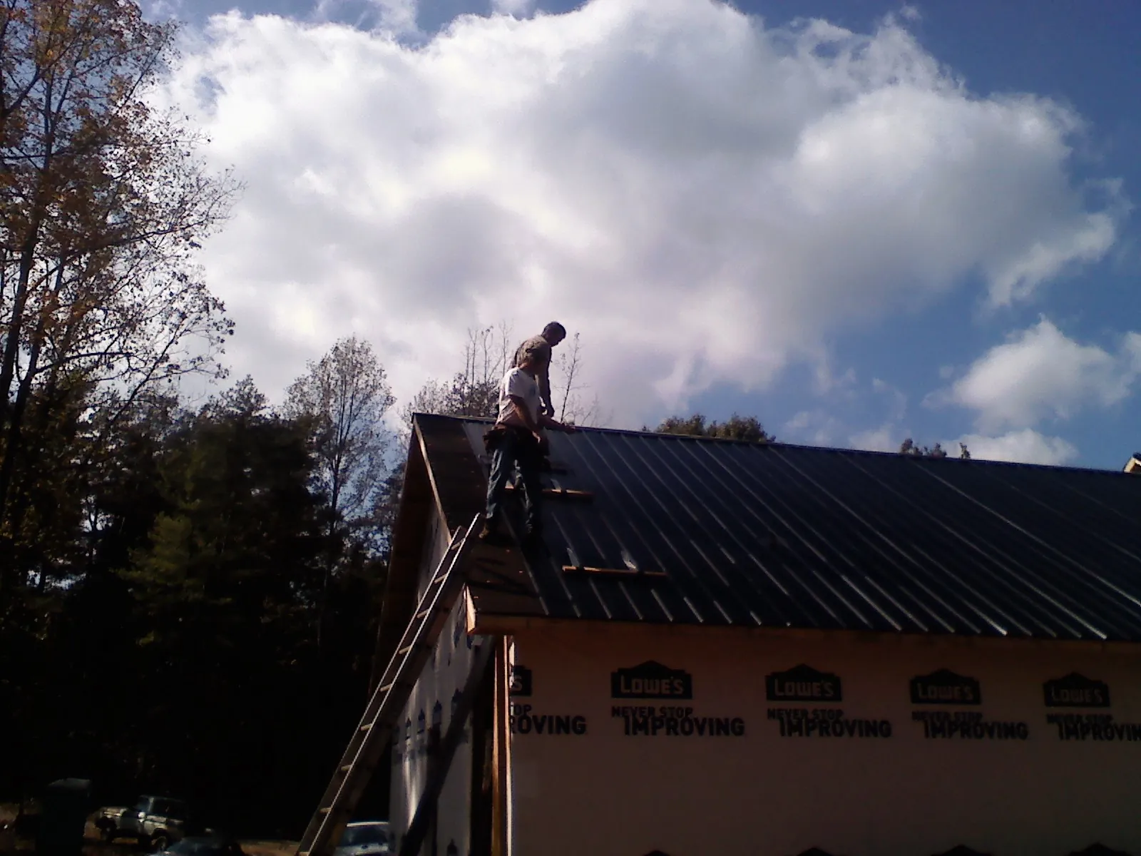 Roofer fastening dark metal panels high against a cloudy sky, from a Roof Inspection job in Huron