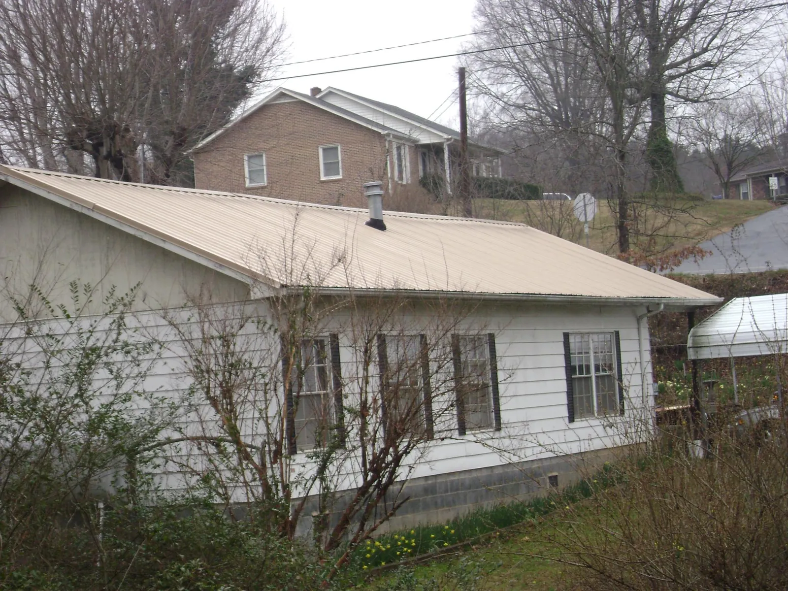 Tan metal roof on a white sided house set into a hillside — Commercial Roofing by Roofing Brothers in Huron