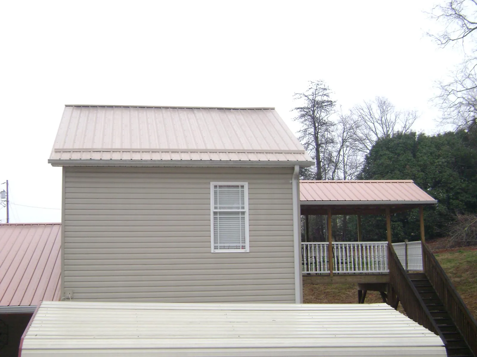 Tan metal roofs on a two story addition and attached porch, from a Roof Replacement job in Huron